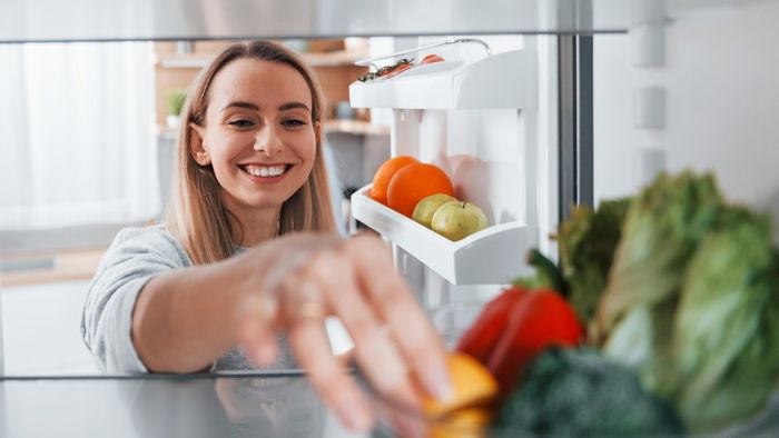 A woman arranges vegetables inside her refrigerator.