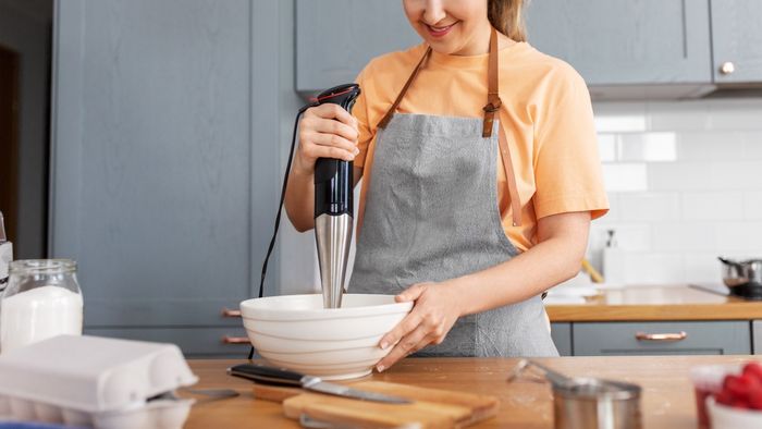 A woman preparing food in her kitchen with an immersion blender.