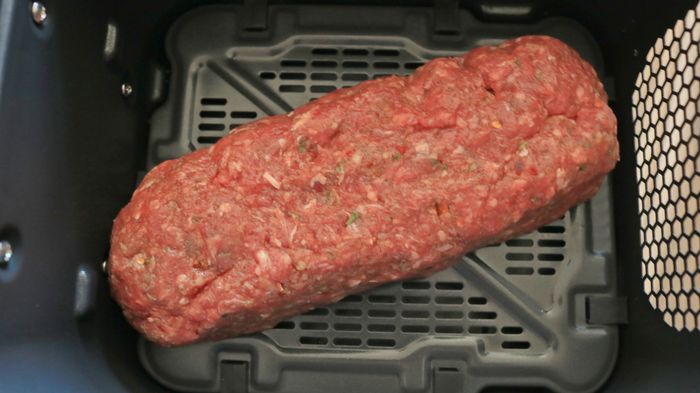 A raw meatloaf placed in the air fryer basket, ready to cook.