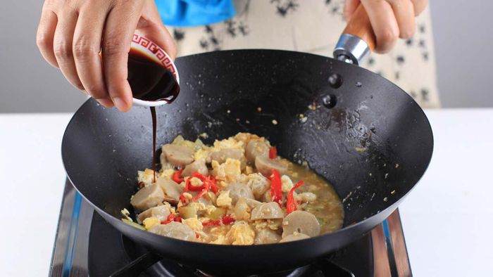 A hand pouring soy sauce into a wok.