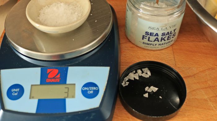 A kitchen scale with a small bowl of salt on it, being measured for weight.
