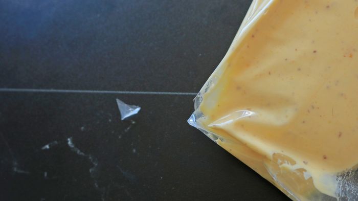 A close-up shot of a plastic bag filled with yellow filling, with the corner snipped off.