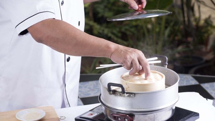 A chef preparing food using a steaming technique.