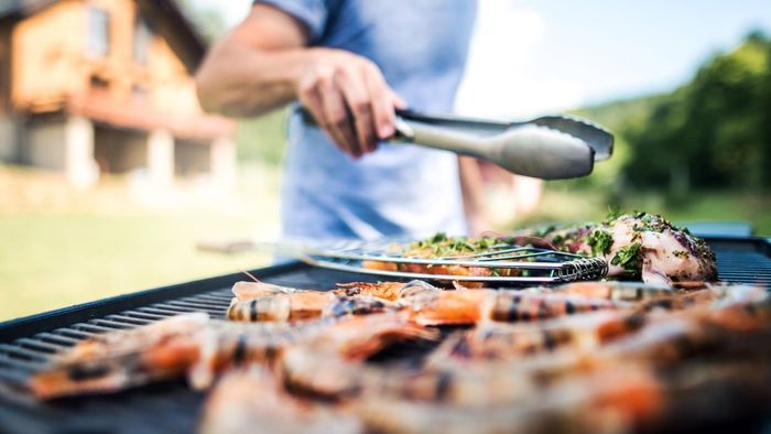 A man's hand holding tongs over an outdoor grill.