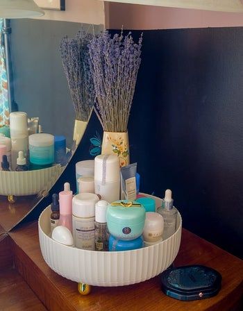 A reviewer's image showing a white tray with gold feet filled with cosmetics, neatly arranged on a beautifully decorated counter.