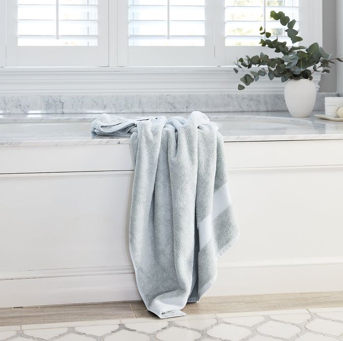 A soft light blue plush bath towel draped over the edge of a bathtub.