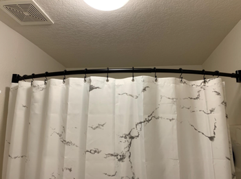 A reviewer's photo of a bathroom featuring a curved shower curtain rod.