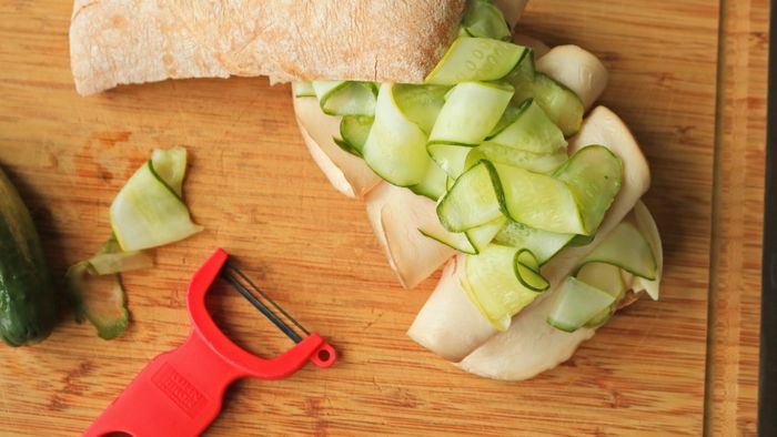 A close-up shot of pickles resting on a sandwich placed on a cutting board.