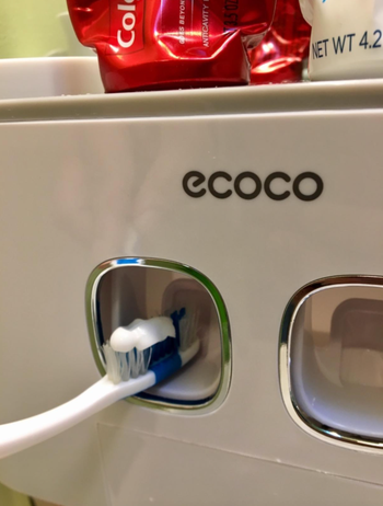 A close-up shot showing a toothbrush receiving toothpaste from the dispenser, illustrating its smooth and efficient operation.