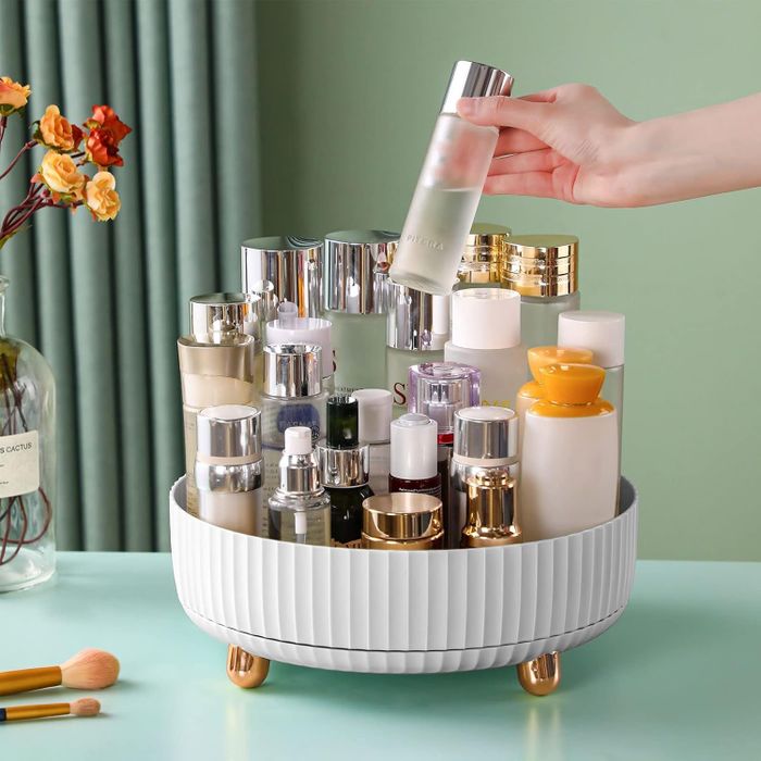 A rotating cosmetic organizer with several skincare bottles on a table. A hand is holding one of the bottles, indicating which product to choose.