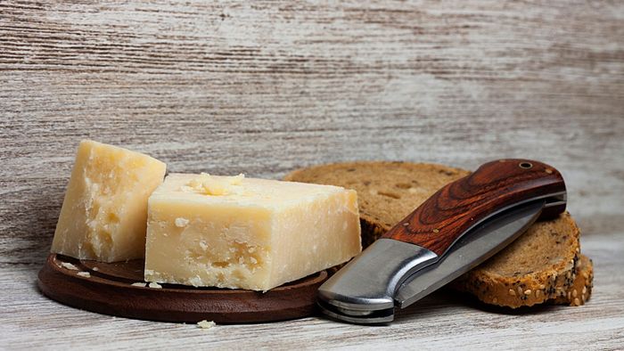 A pocket knife resting on a loaf of bread beside a block of hard cheese.