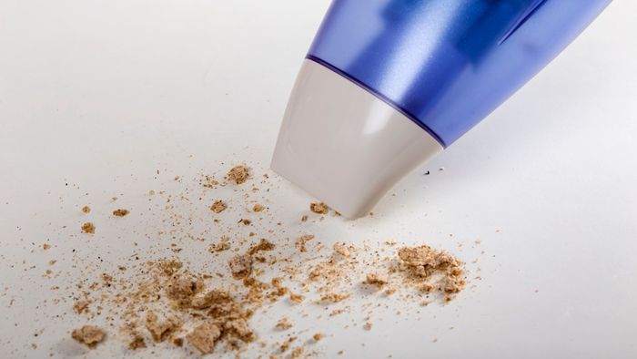 A vacuum clearing crumbs off a white surface.