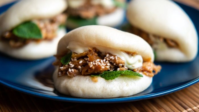 A close-up of gua bao filled with shredded meat resting on a plate.