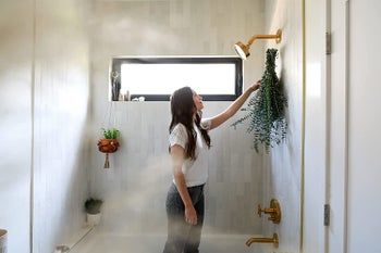 A person is seen standing in a shower, hanging a large bundle of eucalyptus.