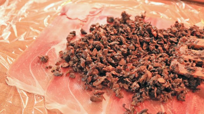 Spreading duxelles over a sheet of prosciutto.