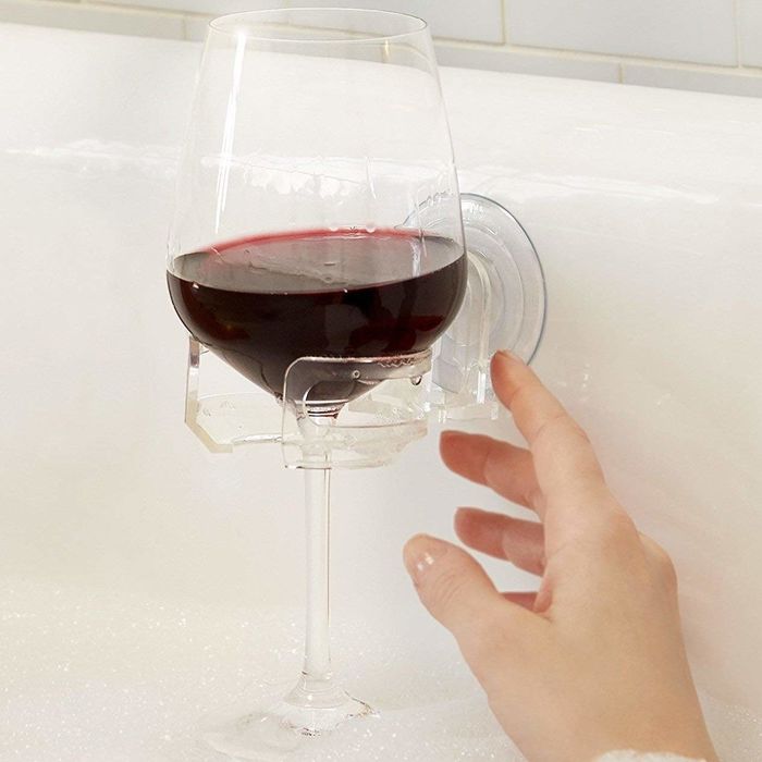 A wine glass resting in a bubble bath, held in place by a suction cup holder on the side of the tub.