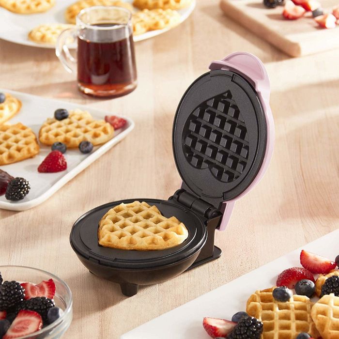 An open mini waffle maker with a heart-shaped waffle cooked perfectly inside.