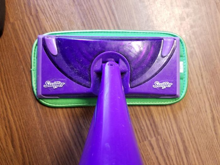 A close-up of a purple Swiffer mop head resting on a wooden floor