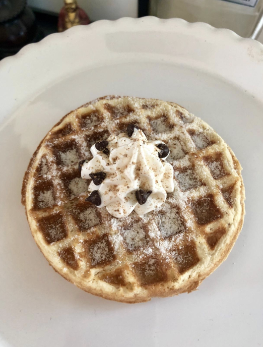 A reviewer's waffle topped with whipped cream and a dusting of powdered sugar.