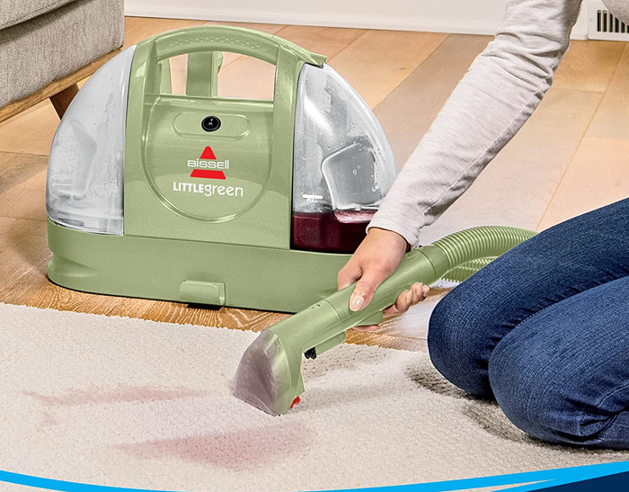 A model using a small green vacuum nozzle to clean a carpet.