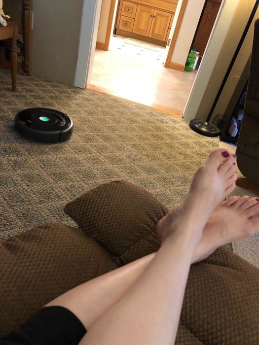 A reviewer relaxing on the couch while their Roomba robot vacuum cleans the floor