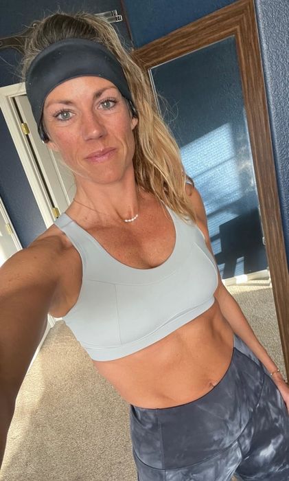 A reviewer captures a selfie in workout gear, donning a sports bra and headband, flashing a small smile and looking ready to hit the gym.