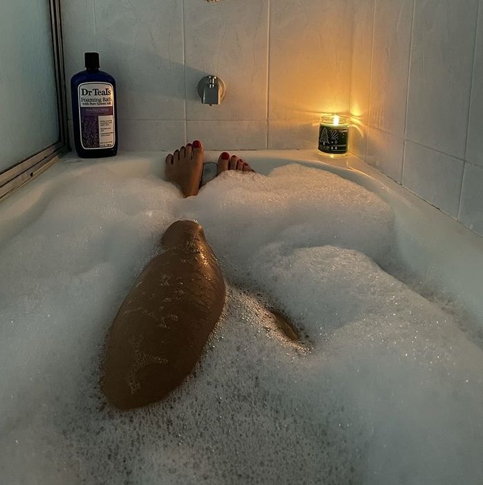 Reviewer relaxing in a bubble bath with a bottle of Dr Teal's placed on the tub's edge.