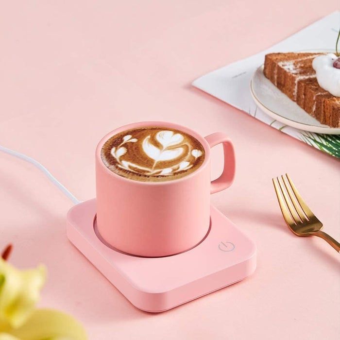 A pink mug warmer on a desk with a steaming mug of coffee placed on top.