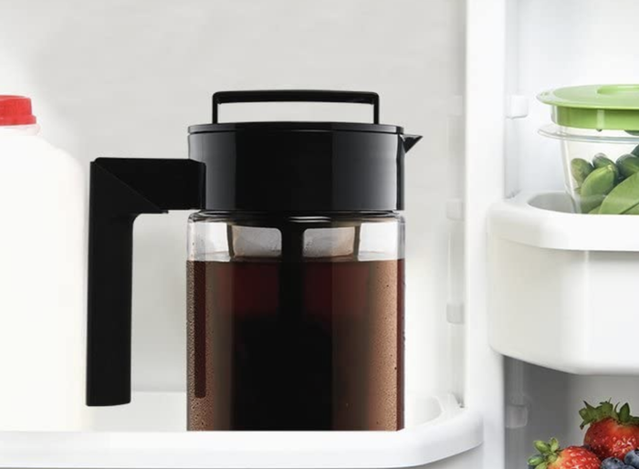 A pitcher filled with iced coffee, equipped with a coffee filter and a large handle, resting in the fridge.
