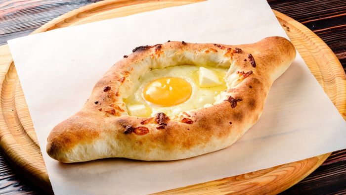 A fresh khachapuri loaf resting on a wooden cutting board