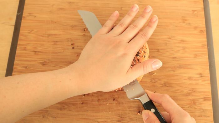 Hands cutting through a bagel.