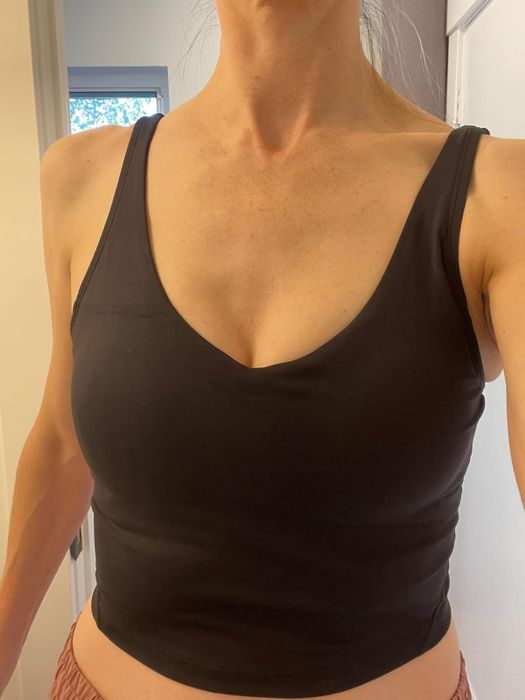 A person modeling a fitted black sleeveless tank top, shown from neck to hips, likely showcasing the garment for a shopping context.