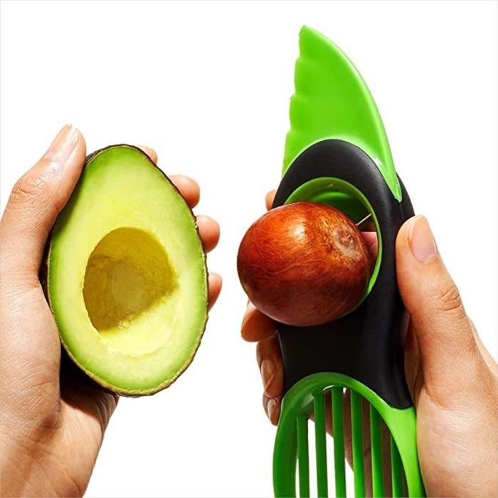 A hand using the avocado tool to remove the pit from an avocado.