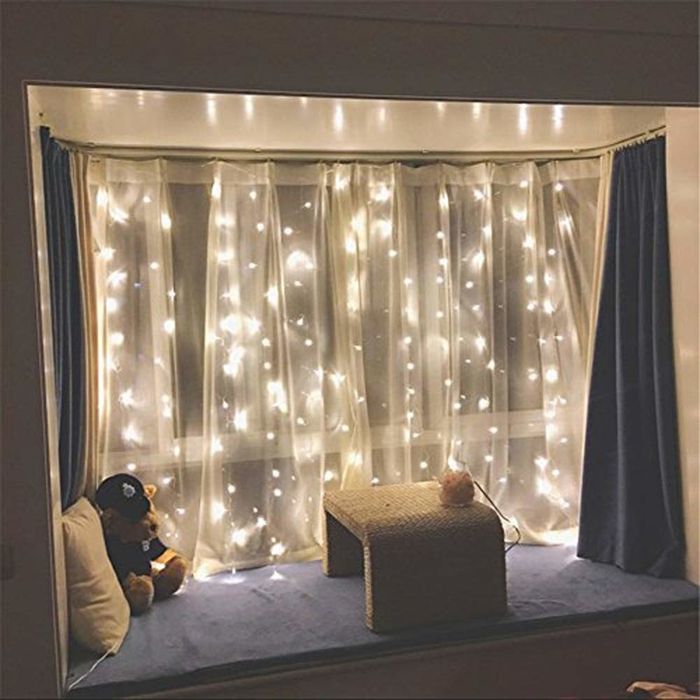 A long strand of fairy lights draped over a window curtain.
