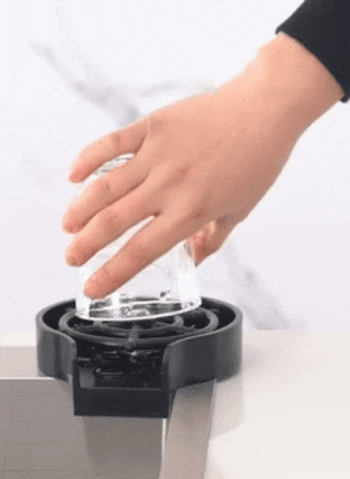 A person using a flat, round rinser to press a cup onto it, causing a powerful jet of water to shoot up into the cup for cleaning.