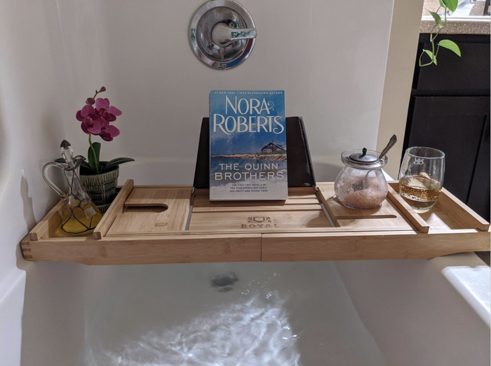 A light wooden display featuring a book, flowers, wine, and olive oil arranged together.