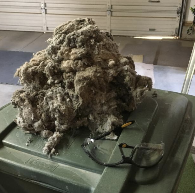 A pile of dryer lint resting on top of a garbage can, with safety glasses placed nearby