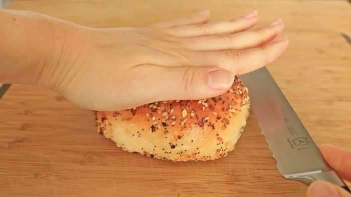 Pressing the bagel down on the table with a knife placed next to it