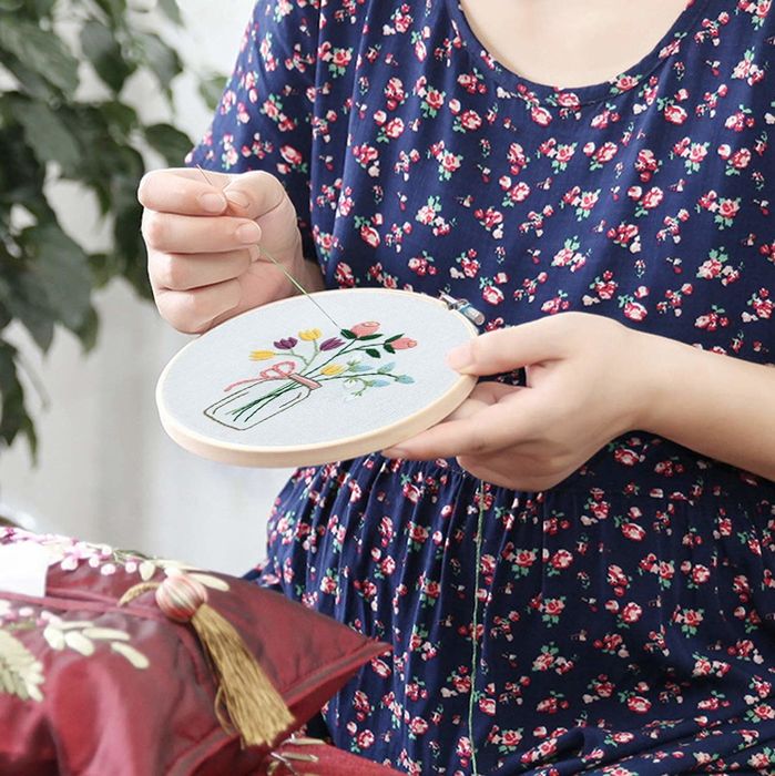 A model carefully stitching a simple flower design into a hoop.