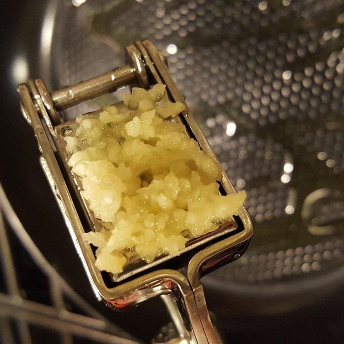A handheld garlic press mashing a garlic clove into a smooth, thick paste.