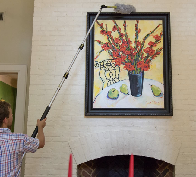 Model using an extendable high-reach duster to clean a hanging portrait
