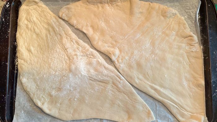 Two pieces of pizza dough laid out on a baking sheet