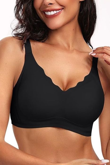 A model is seen wearing a black bra with scalloped edges, smiling as she gently touches the strap with her fingers.