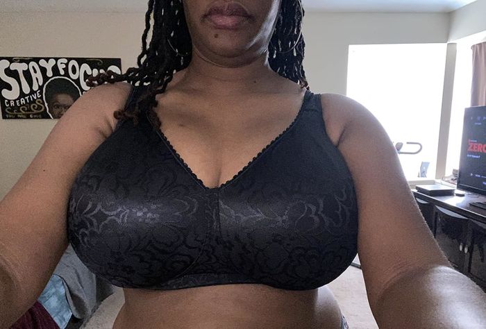 A person takes a selfie while sporting a black patterned sports bra. A poster with partial text reading 