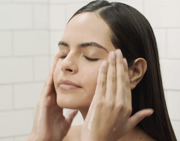 A model is applying the CeraVe hydrating facial cleanser on their face.