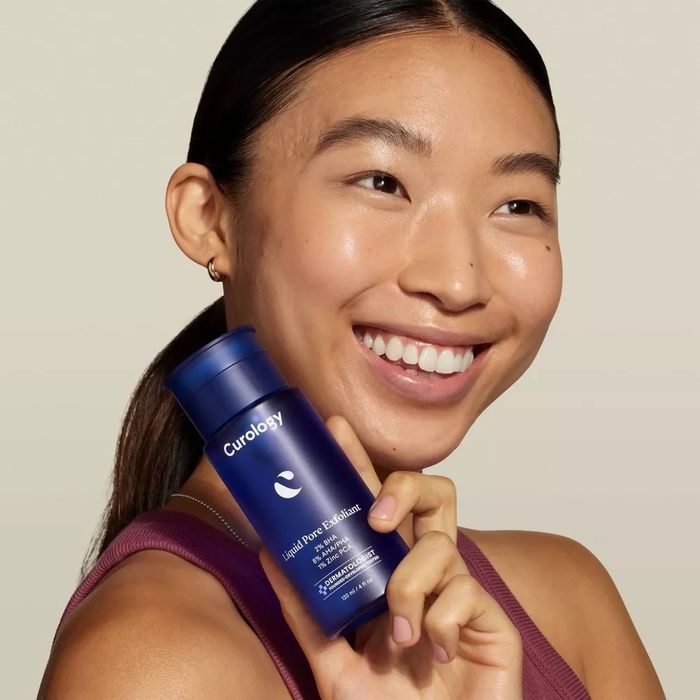 A model is showcasing a bottle of Curology's liquid pore exfoliant.