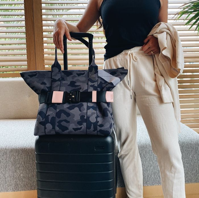 A model standing beside a suitcase with a bag on top, secured with a travel belt