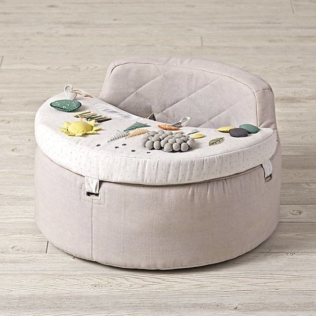 A light pink/gray soft chair with a tray filled with soft toys for a baby to play with.