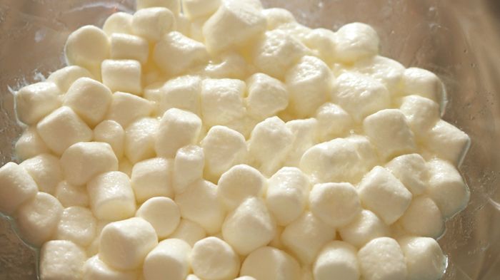 Mini marshmallows mixed with butter in a transparent bowl.