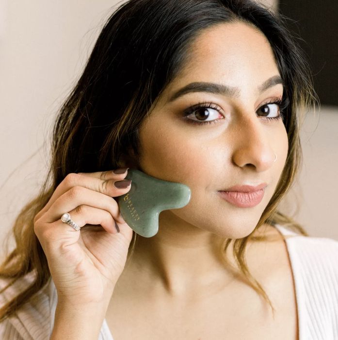 A model is using a jade gua sha tool to massage their face.